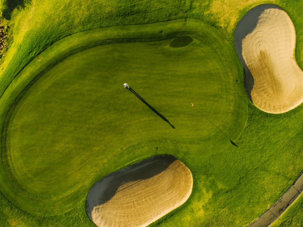 Aerial view of players on a green golf course. Golfer playing on putting green on a summer day.